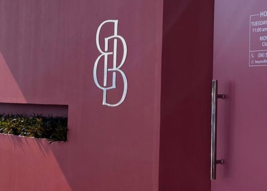 Entrance to Beyond Beauty, Ajman, AE, featuring sleek design and logo on a modern maroon facade.