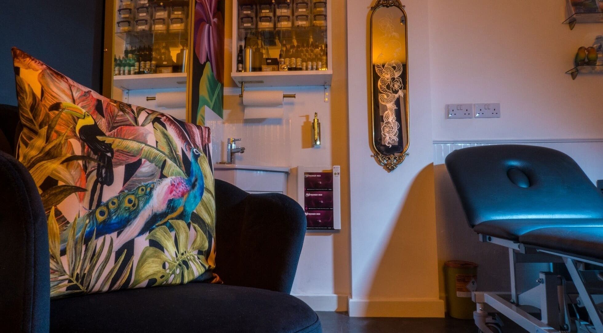 Relaxing corner at Lucky Bird Tattoo Studio, Somerton, England, GB featuring a vibrant tropical pillow and sleek tattoo chair.