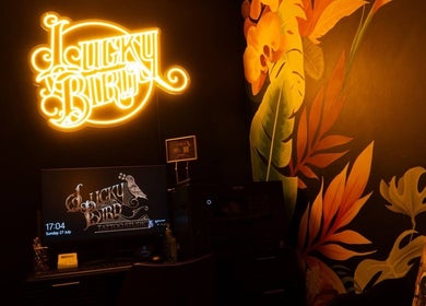 Vibrant neon sign in Lucky Bird Tattoo Studio, Somerton, England, GB with artistic mural and workspace.