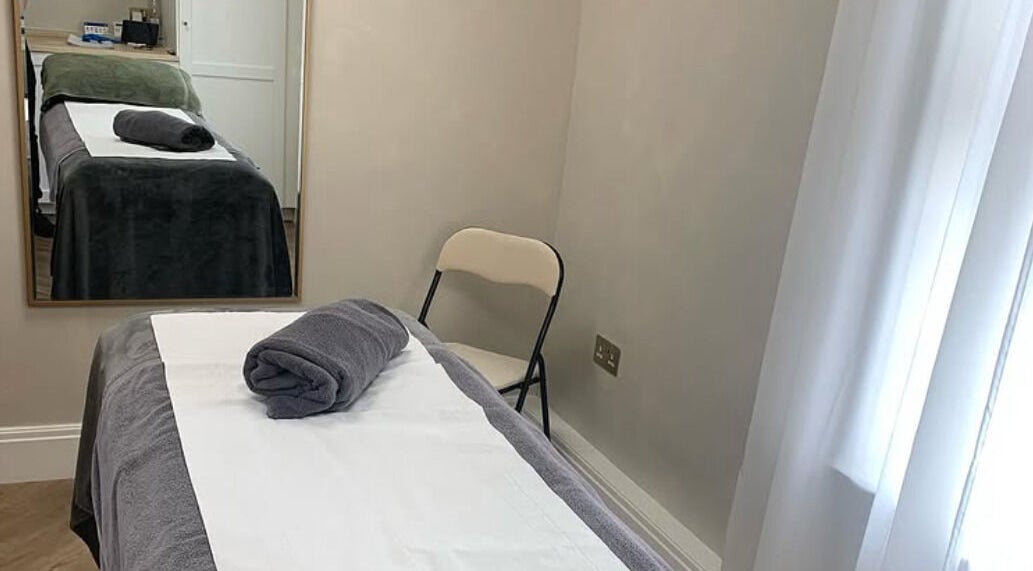 Tranquil treatment room at ReJENerate Body Clinic, Worsley, England, GB, featuring a massage table and folded linens.