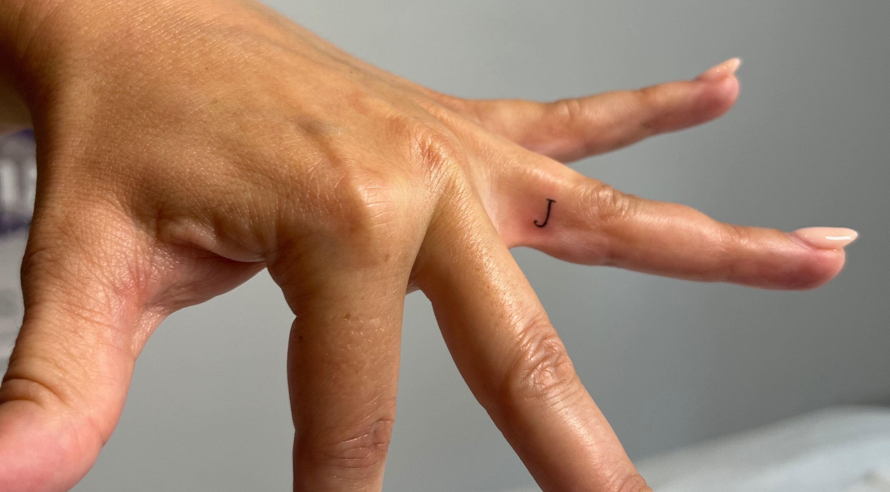 Elegant minimalist letter tattoo on finger at Jenny Jones Ink & Aesthetics, East Grinstead, England, GB.
