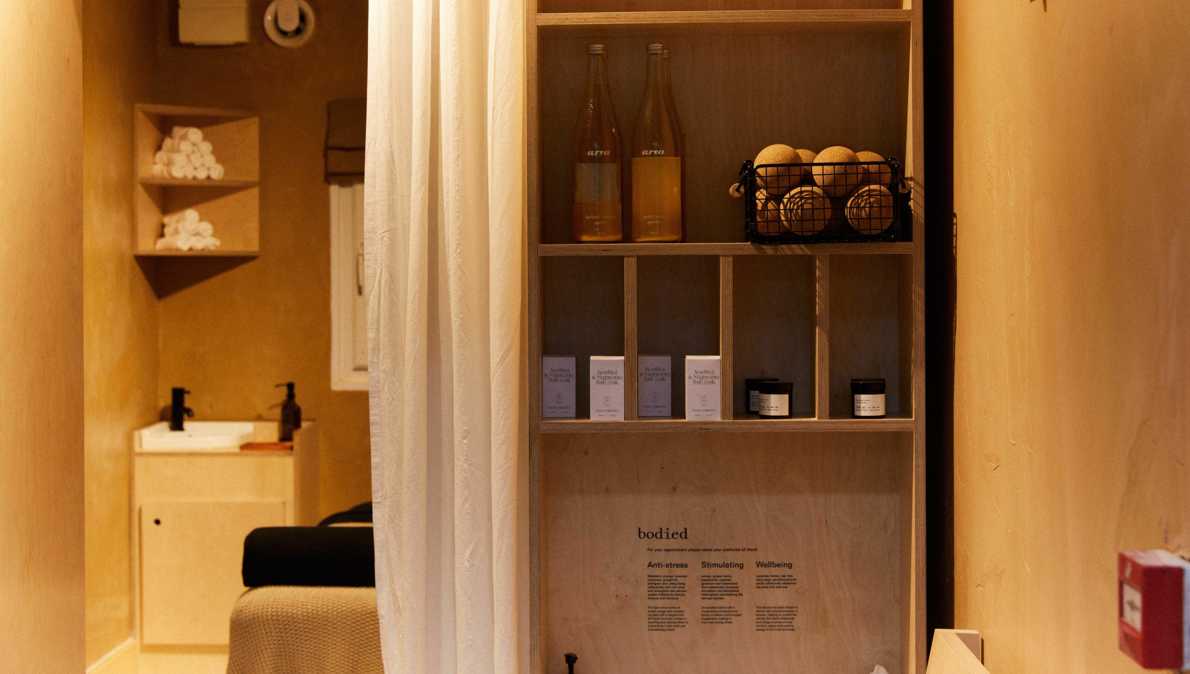 Cozy, earthy-toned treatment room at Bodied, London, England, GB, featuring wellness products and towels.
