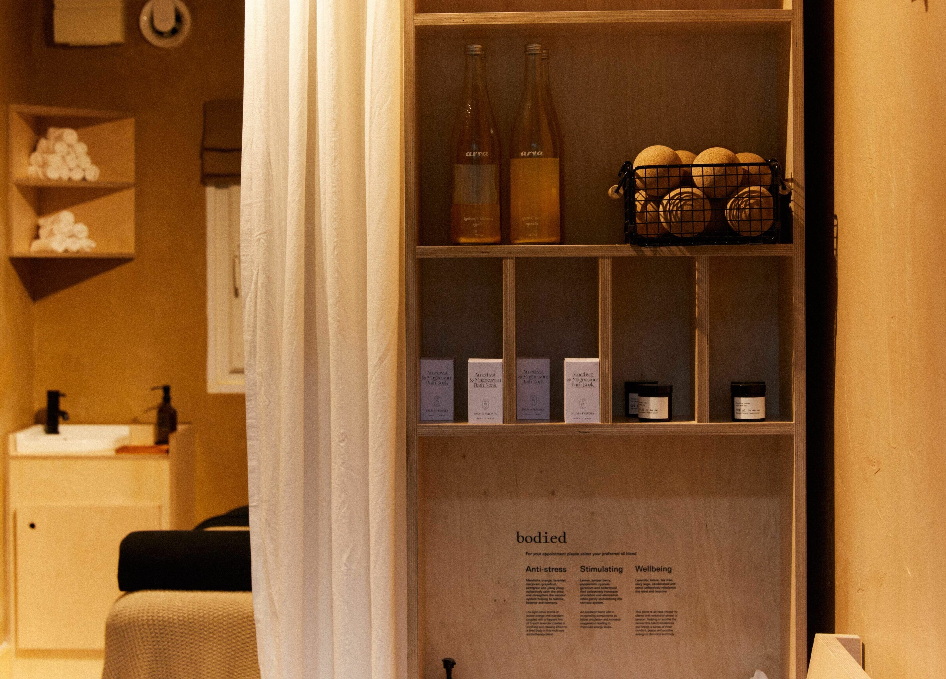 Cozy, earthy-toned treatment room at Bodied, London, England, GB, featuring wellness products and towels.