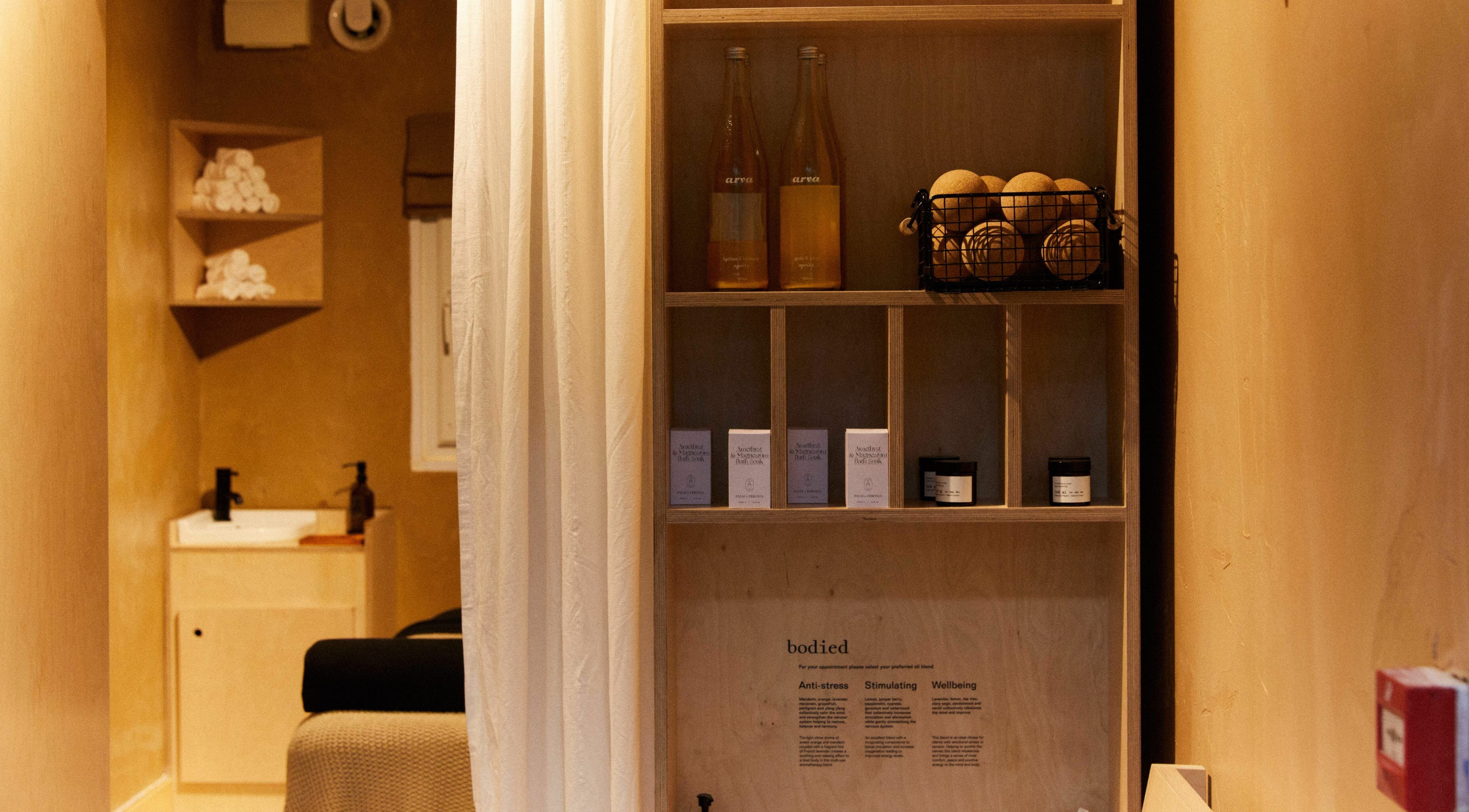 Cozy, earthy-toned treatment room at Bodied, London, England, GB, featuring wellness products and towels.