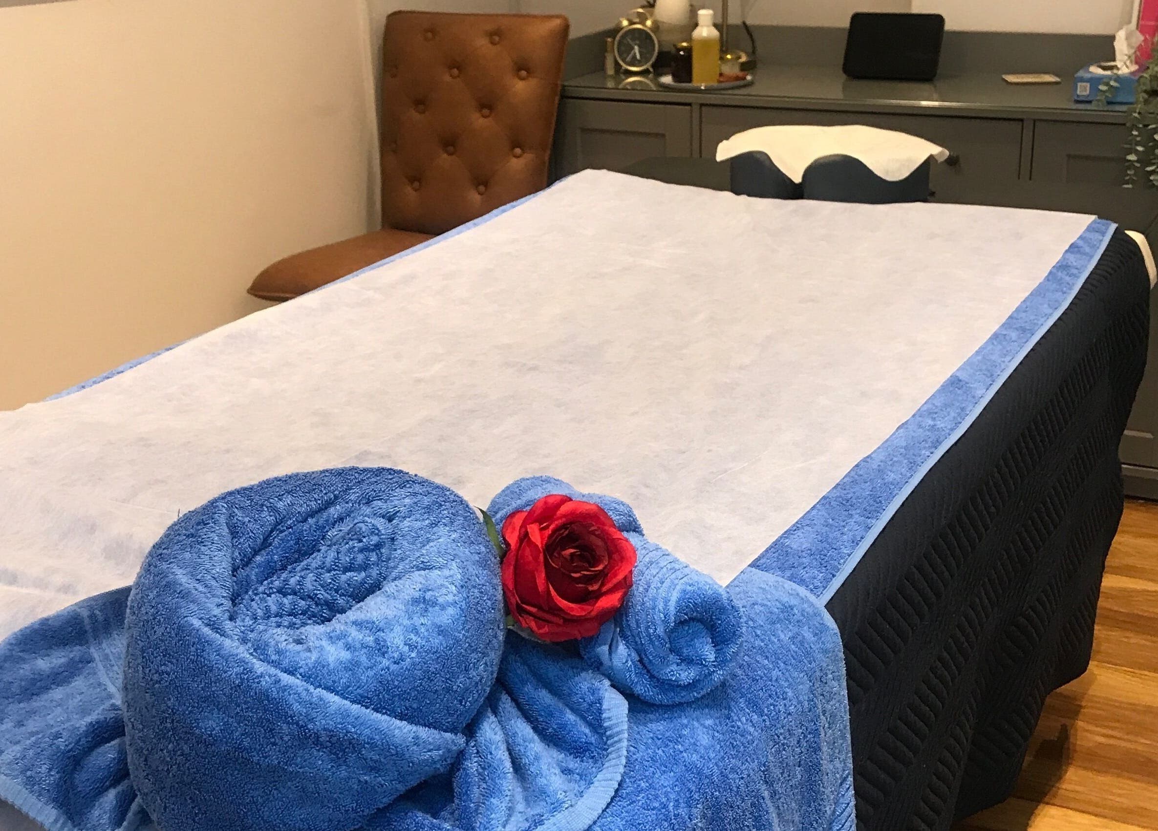 Cozy massage room at Thawee Thai Therapy, Solihull, England. Blue towels and red rose on treatment table.