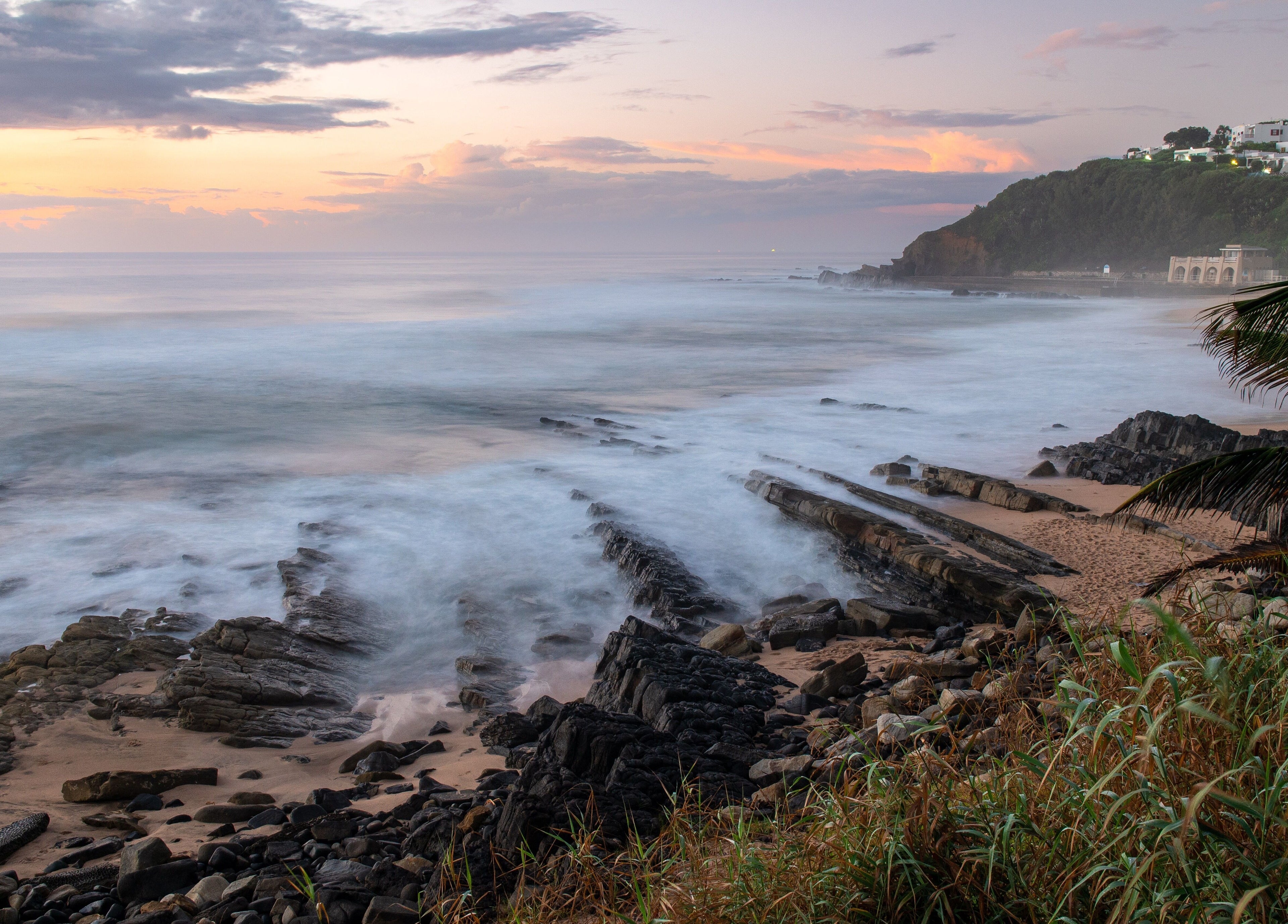 Tranquil ocean view near Sala Beach Spa, Dolphin Coast, KwaZulu-Natal, ZA. Waves gently lap rocky shoreline at sunset.