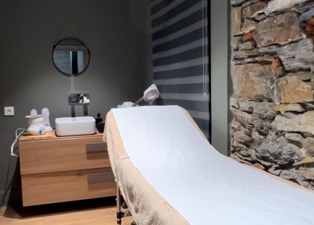 Salle de soin relaxante à L’instant D’une Pause, Bastia, Corse, FR avec table de massage et mur en pierre.
