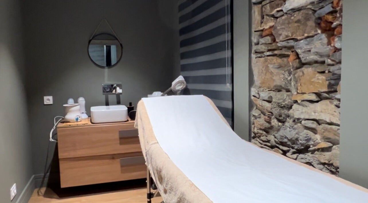 Salle de soin relaxante à L’instant D’une Pause, Bastia, Corse, FR avec table de massage et mur en pierre.