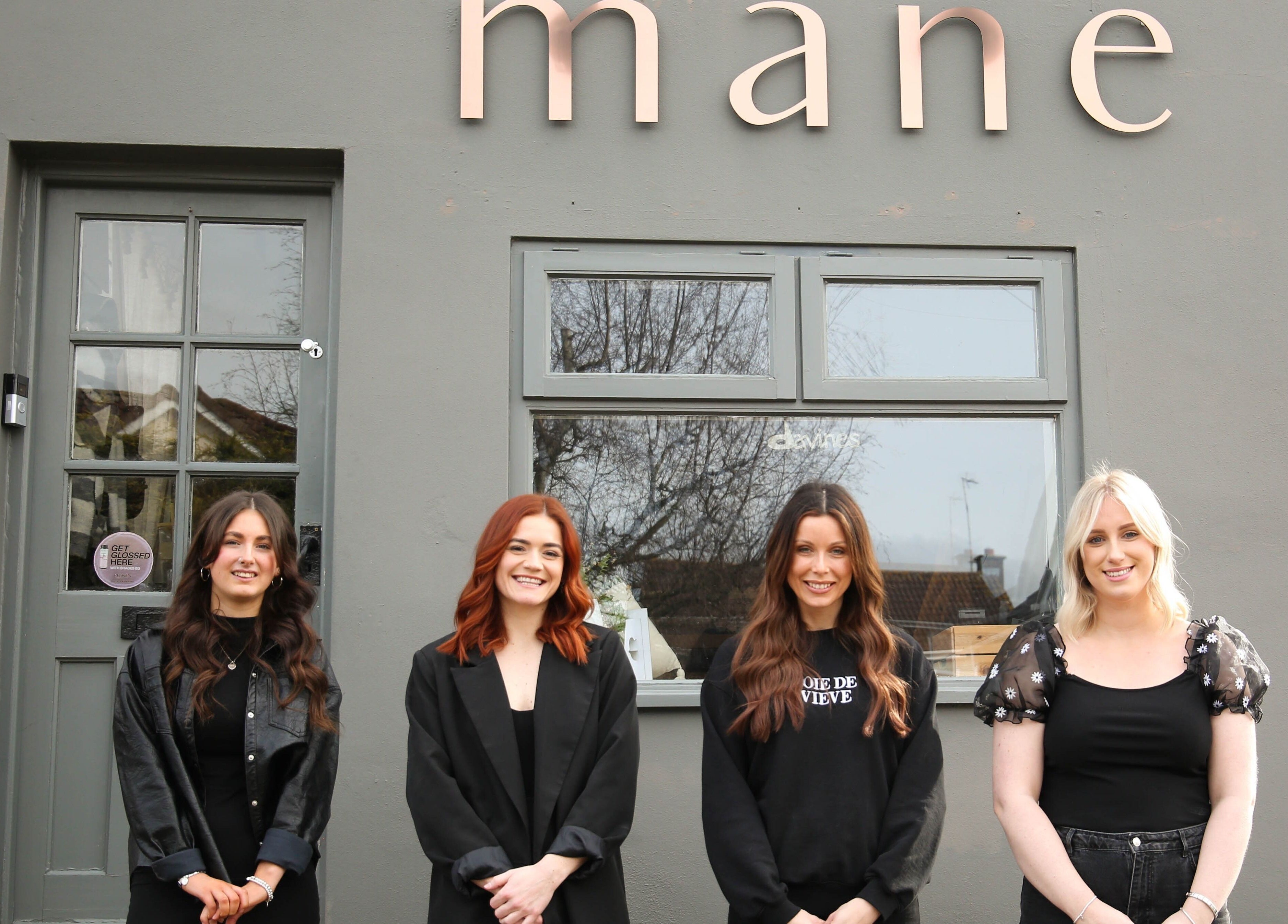 Team of stylists at Mane beauty salon, Huncote, England, GB, standing outside gray entrance.