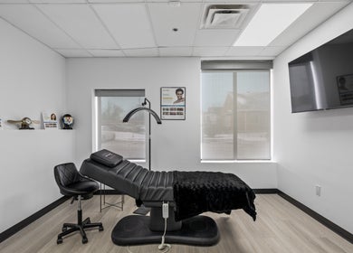 Modern treatment room at Beauty Matched Med Spa, Sarnia, Ontario, CA featuring a sleek black chair and large TV.