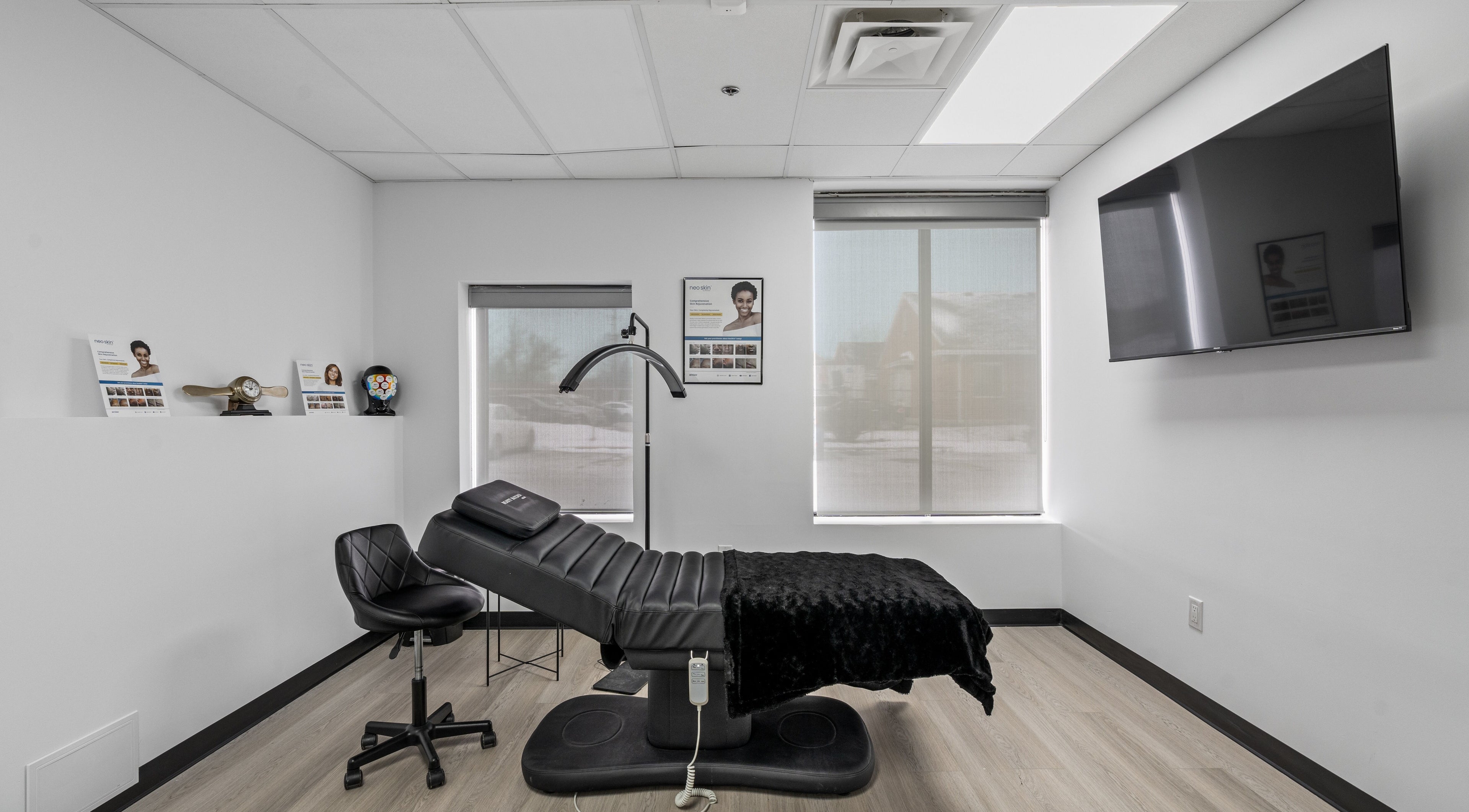 Modern treatment room at Beauty Matched Med Spa, Sarnia, Ontario, CA featuring a sleek black chair and large TV.