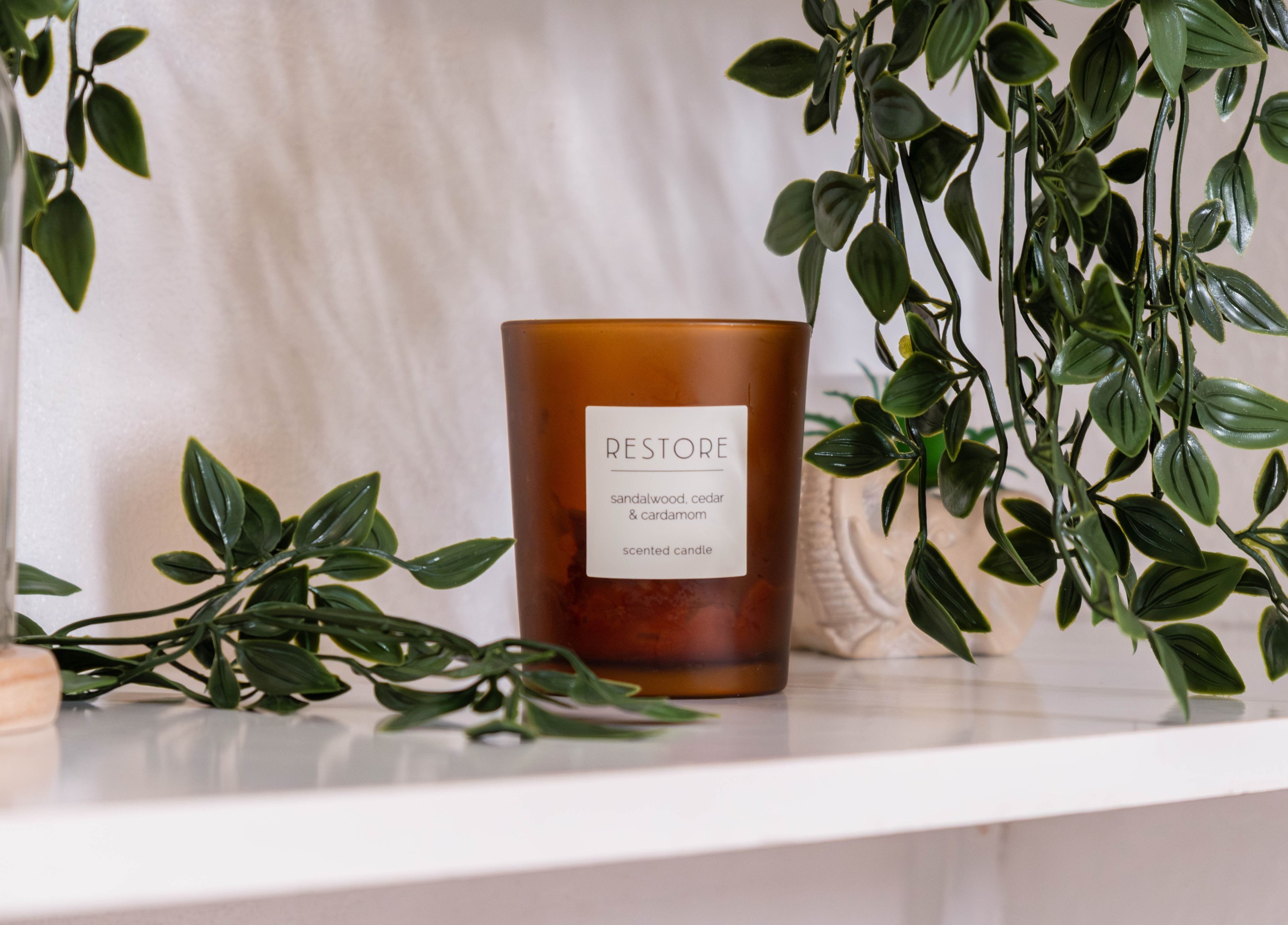 Sandalwood candle on a shelf at Arieyes, London, England, GB with lush greenery for a soothing ambiance.