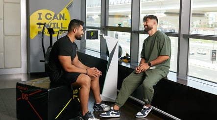 Two men converse at Justfit EMS Dubai, Dubai, AE, enhancing wellness with cutting-edge equipment.
