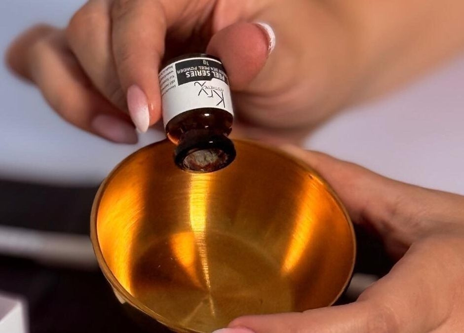 A person pouring essential oil into a golden bowl at Fina, B kara, MT.