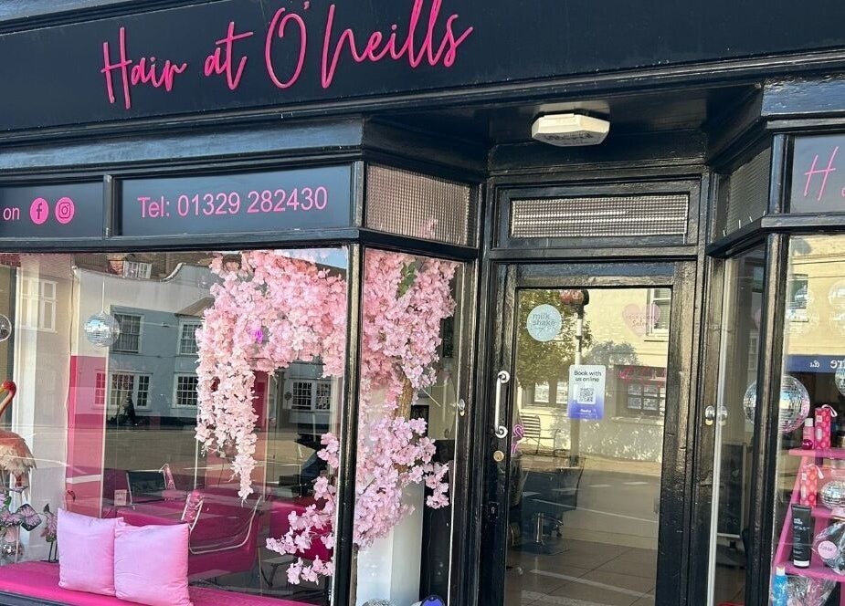 Exterior view of Hair at O’Neills in Fareham, England, GB, showcasing pink decor and inviting displays.