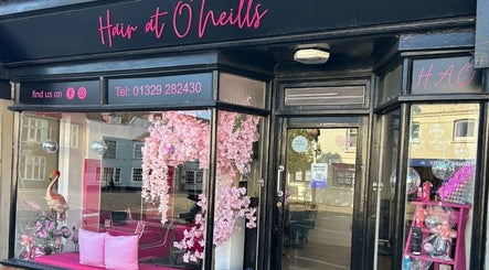Exterior view of Hair at O’Neills in Fareham, England, GB, showcasing pink decor and inviting displays.
