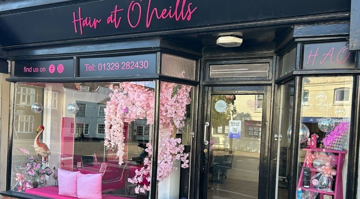 Exterior view of Hair at O’Neills in Fareham, England, GB, showcasing pink decor and inviting displays.