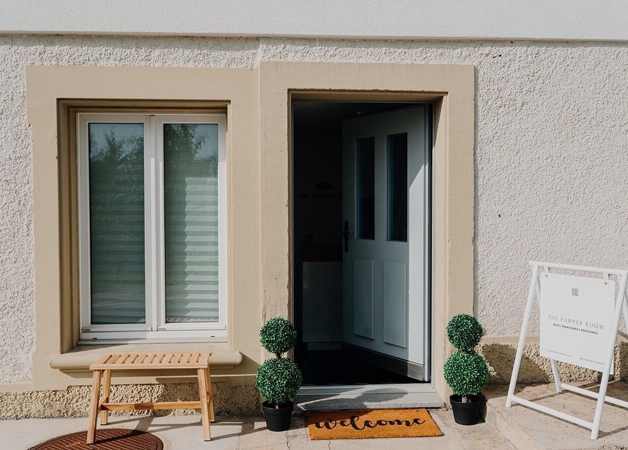 Welcoming entrance of The Pamper Room, Bern, Switzerland, CH with a 'welcome' mat and greenery.