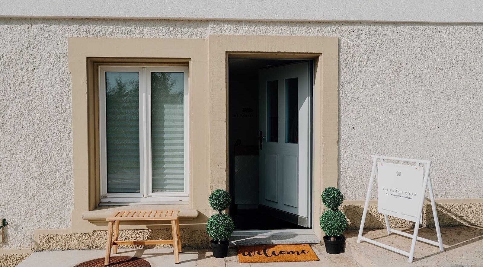 Welcoming entrance of The Pamper Room, Bern, Switzerland, CH with a 'welcome' mat and greenery.