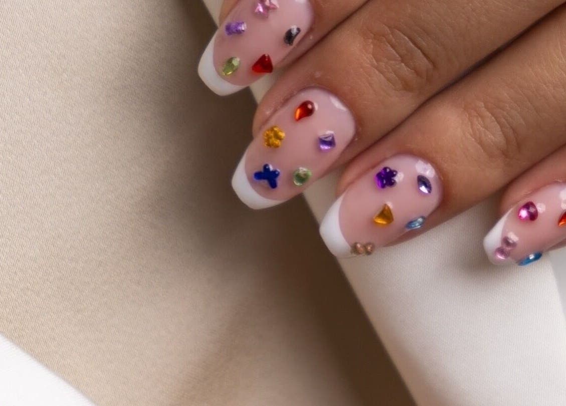 Vibrant gemstone nail art by Hello Lashes, Riyadh, Riyadh Province, SA. Stunning design on a soft beige fabric.