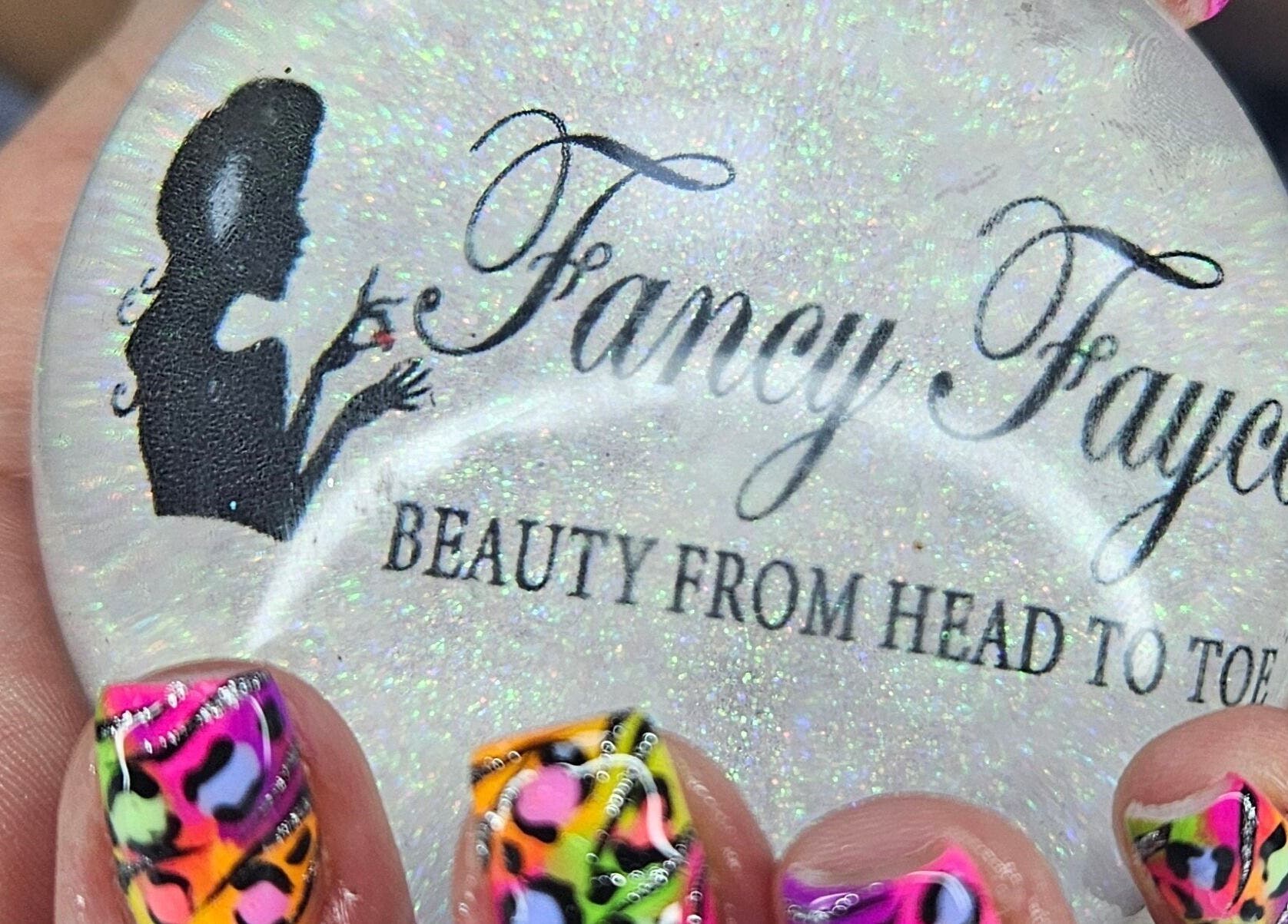 Close-up of vibrant nail art holding Fancy Fayce logo orb at beauty venue in Huddersfield, England, GB.