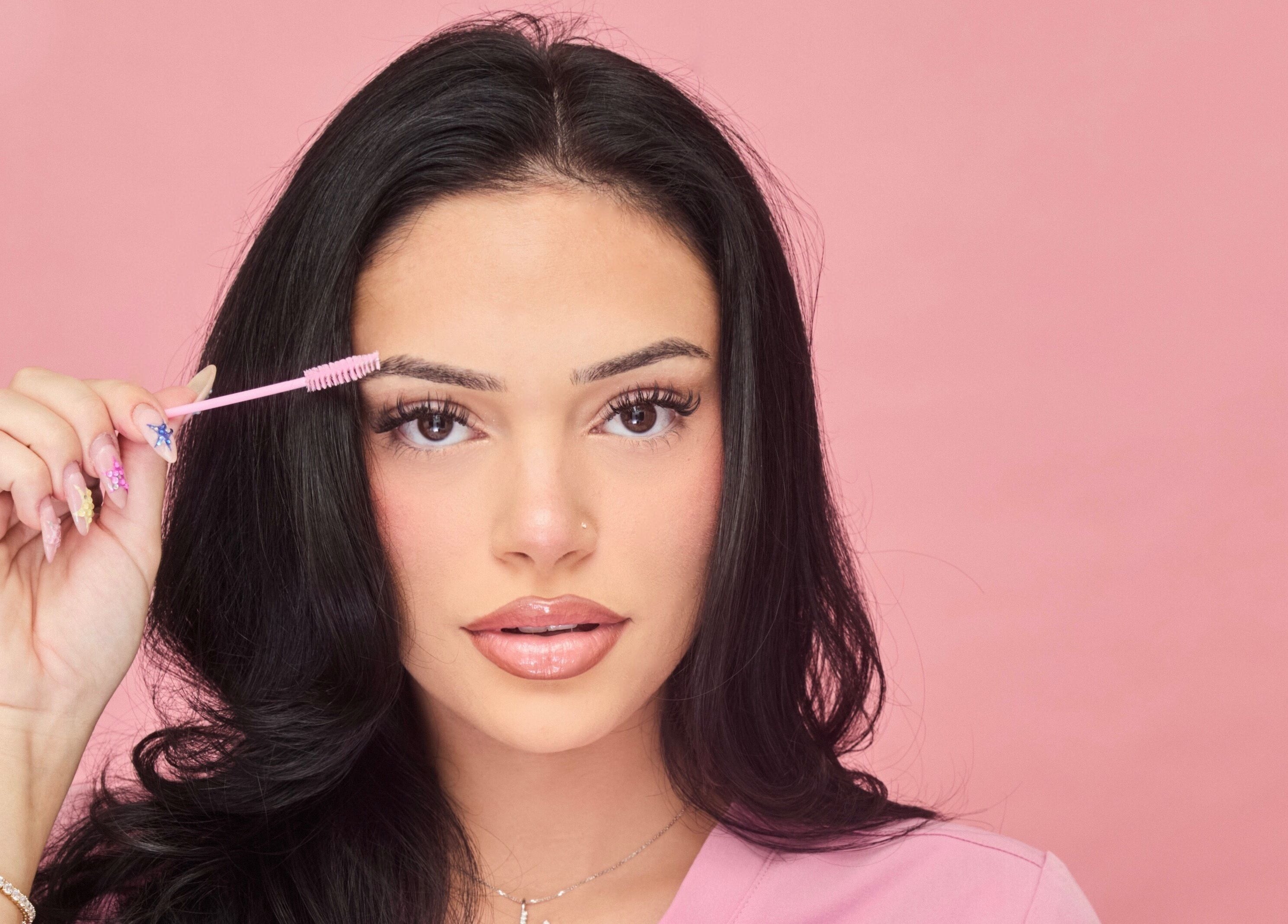 Woman styling brows at Victoria | Lashed Out by Vic in Vaughan, Ontario, CA. Pink background enhances beauty focus.