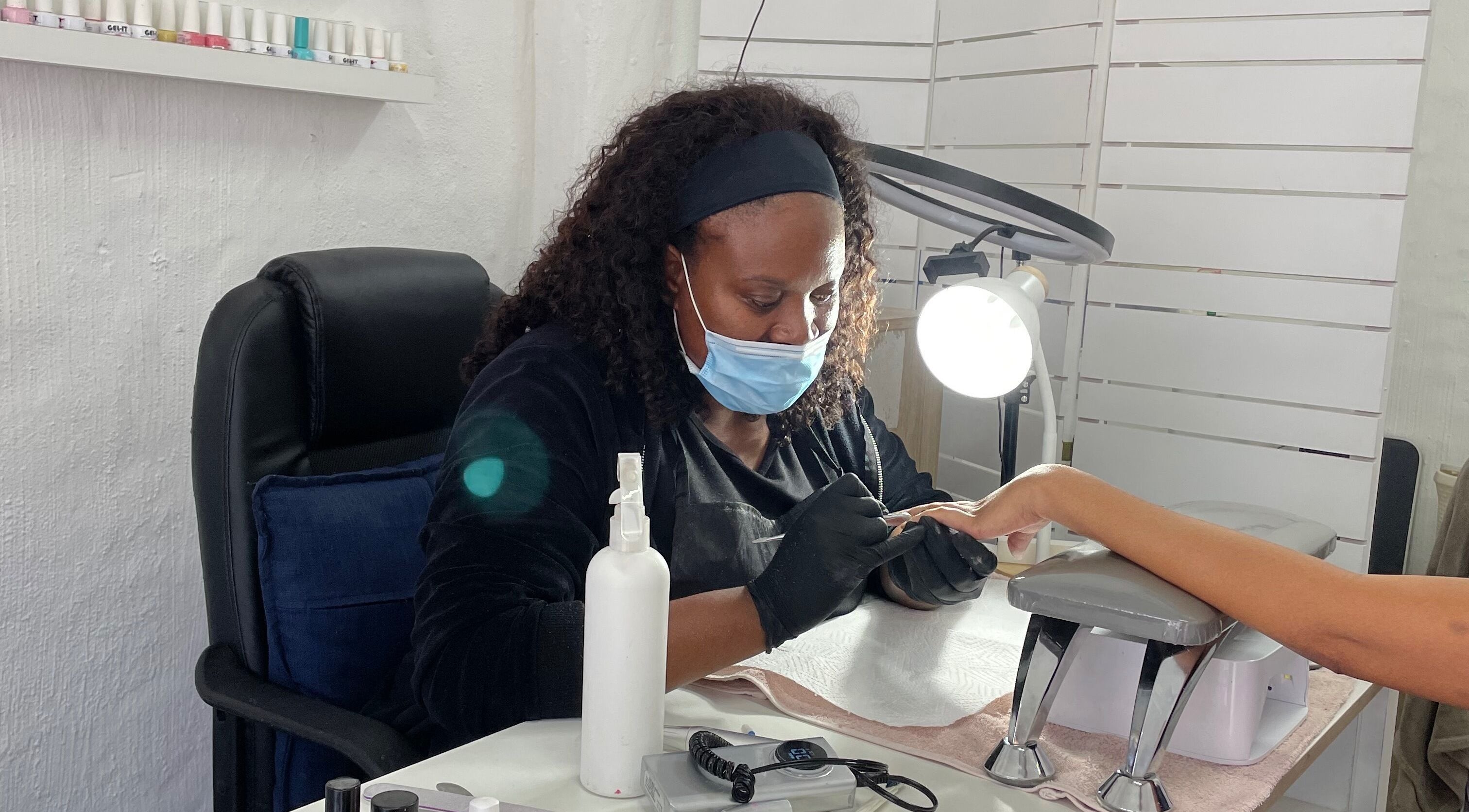 Nail technician at Fab Beauty Boutique, Pretoria, Gauteng, ZA, perfects client's nails under focused light.