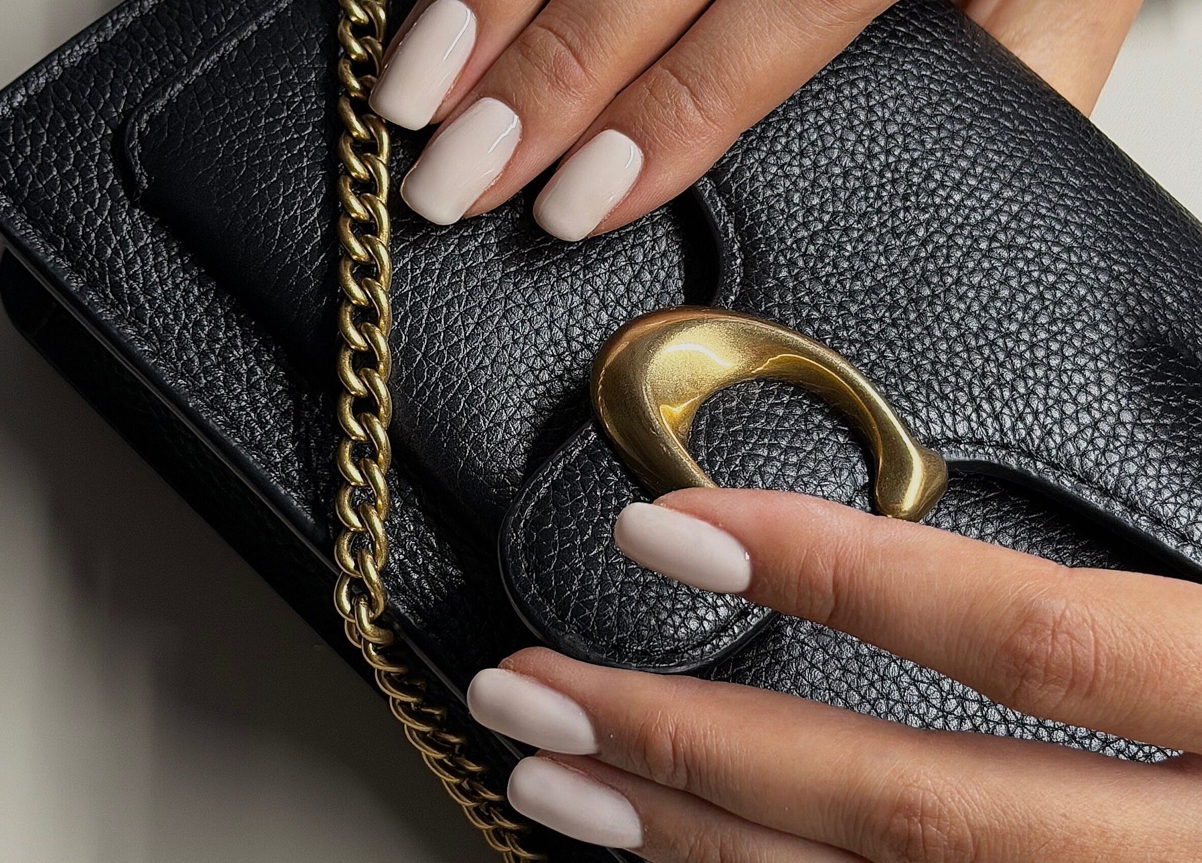 Elegant white manicured nails on a black leather clutch at The Sulking Room, Horsham, England, GB.