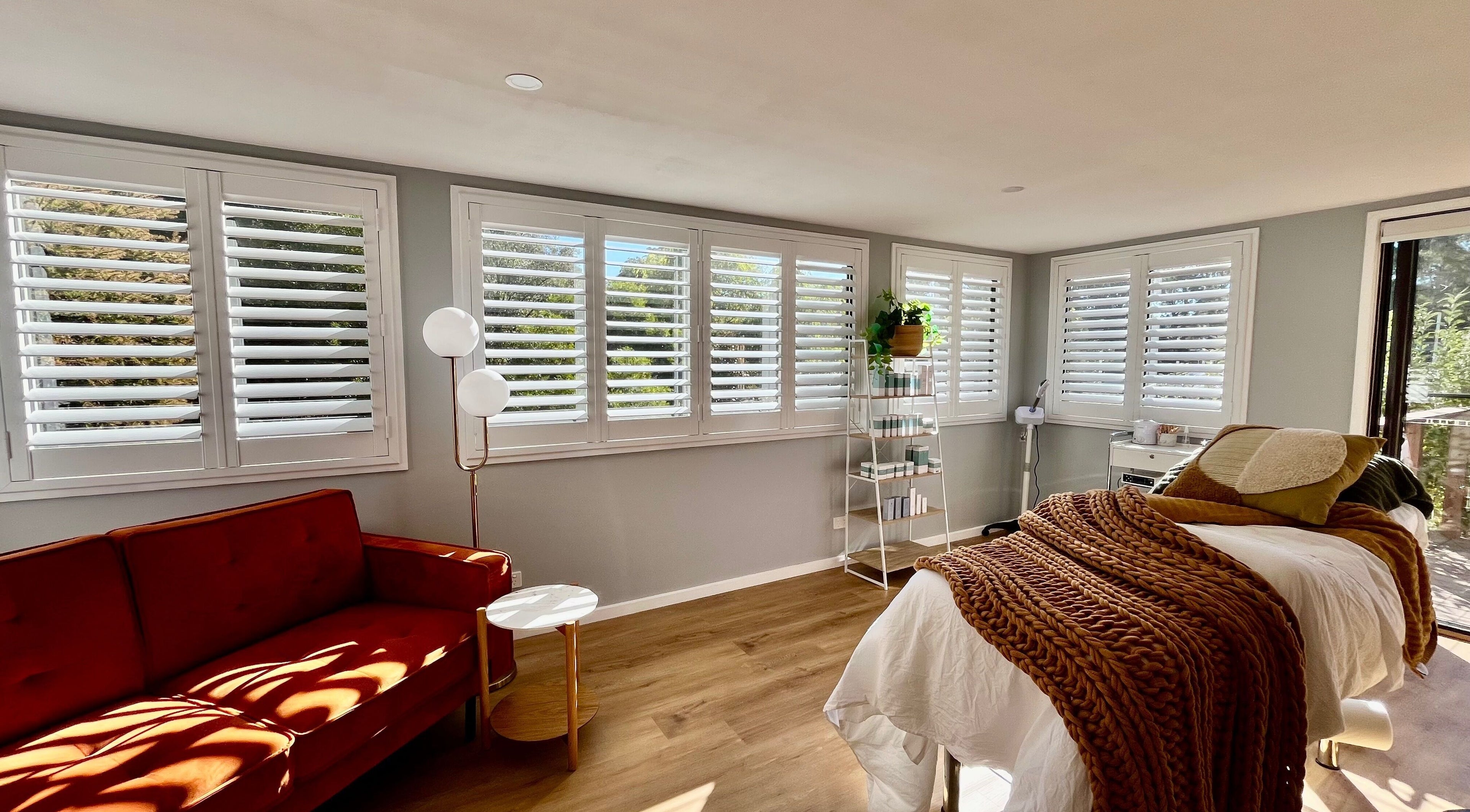 Bright treatment room at Skin Solace in Blackwood, Victoria, AU with cozy bed, red sofa, and light-filled windows.