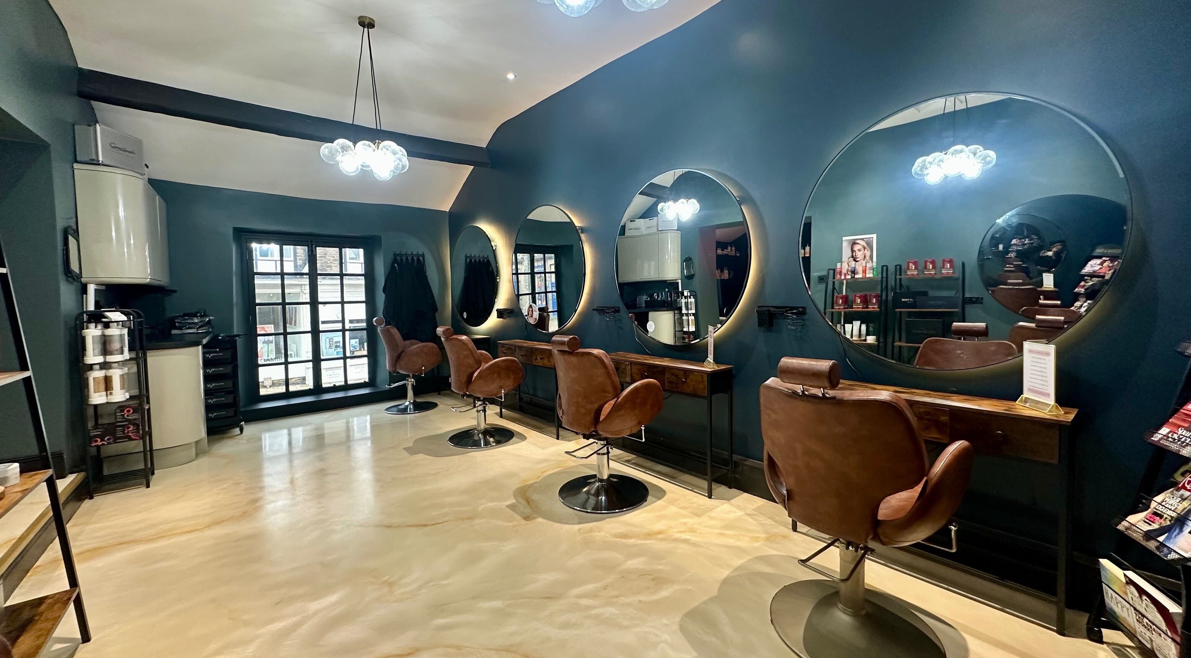 Stylish interior of The Hair & Makeup Project in Ilkley, England, GB with brown chairs and round mirrors.