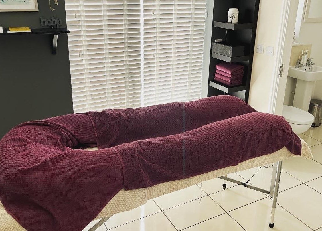 Elysian Therapies massage table in South Ockendon, GB, ready for relaxation with plush maroon towels.
