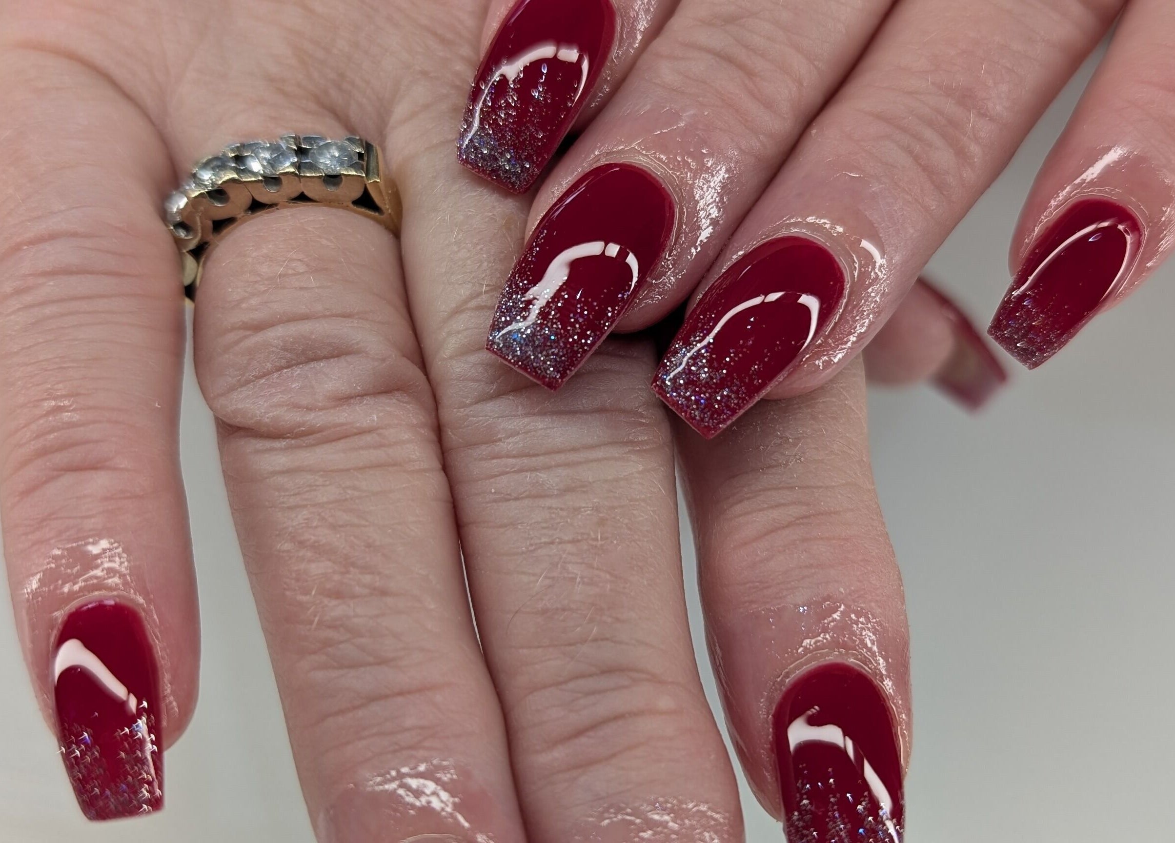 Shiny burgundy nails with glitter tips, styled at Beyond Beauty in Blyth, England, GB.