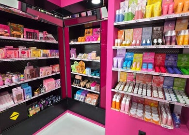 Πολύχρωμα προϊόντα ομορφιάς στο W7 Make Up Professional, Αχαρνές, GR, σε φωτεινά ροζ ράφια.