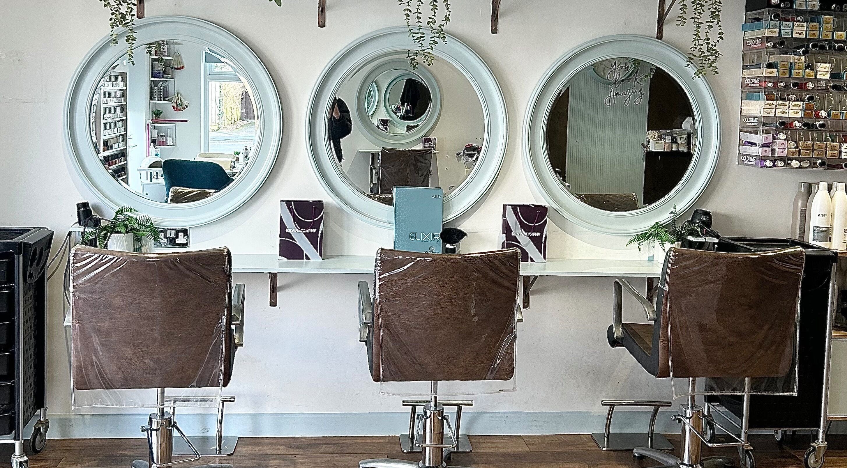 Modern salon interior at Elite Hair and Beauty, Threemilestone, England, GB with circular mirrors and stylish chairs.