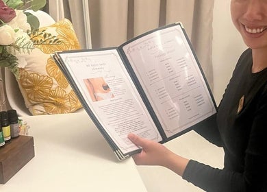 Friendly staff showing treatment menu at Nadesico Beauty & Healing, Singapore, SG with aromatherapy oils in view.