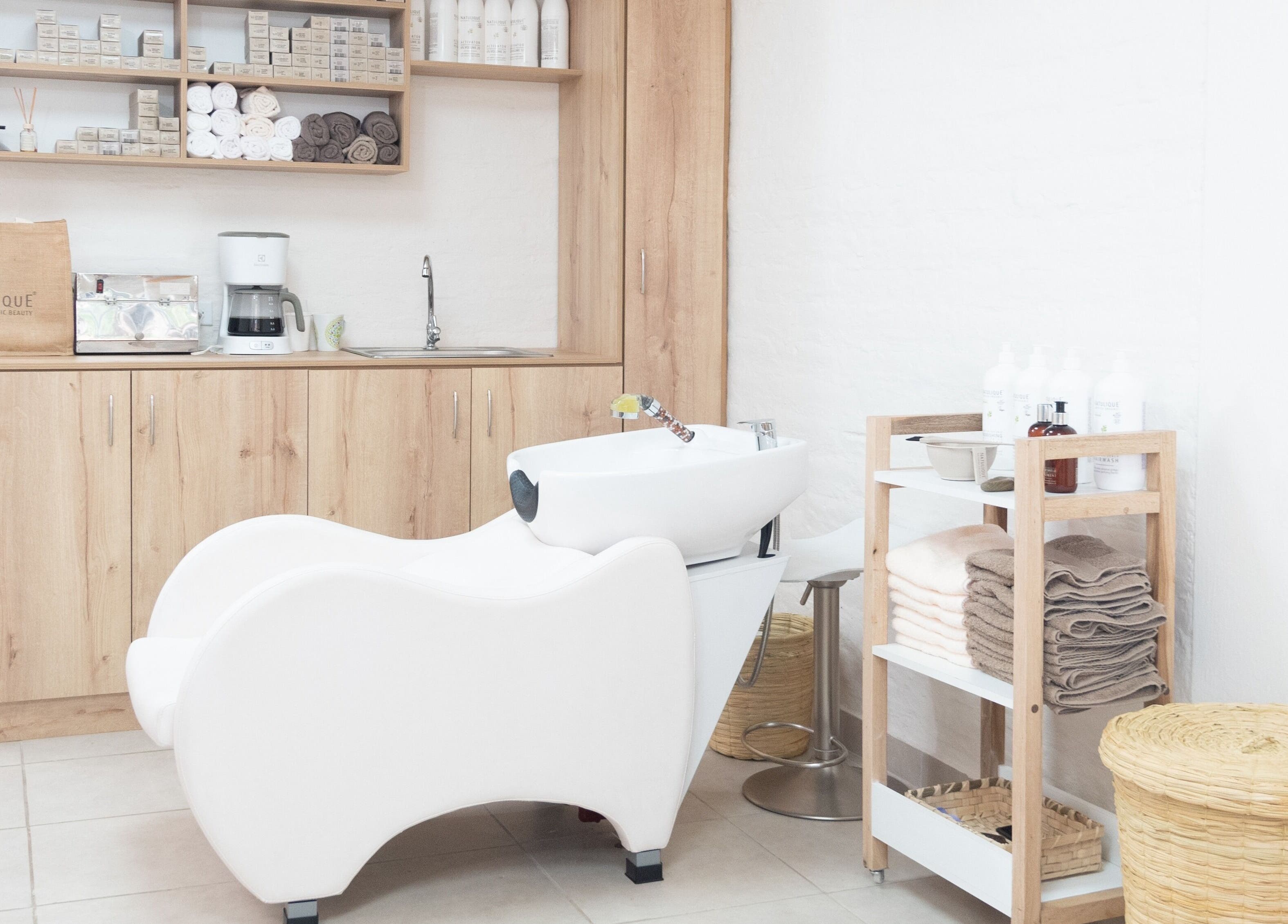 Área de lavado moderna en OKO - Belleza con Propósito, Quito, Ecuador, EC, con silla blanca y muebles de madera.