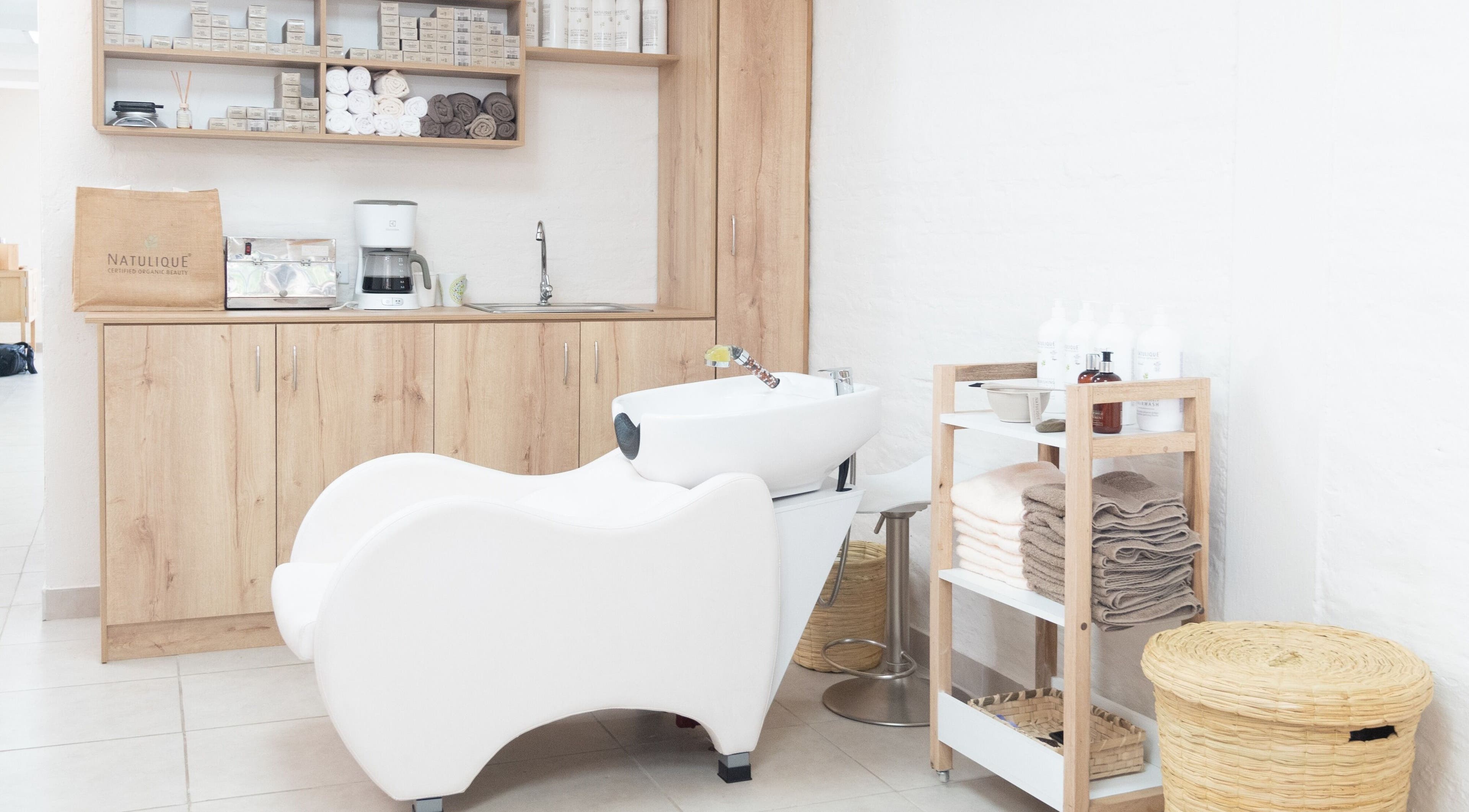 Área de lavado moderna en OKO - Belleza con Propósito, Quito, Ecuador, EC, con silla blanca y muebles de madera.