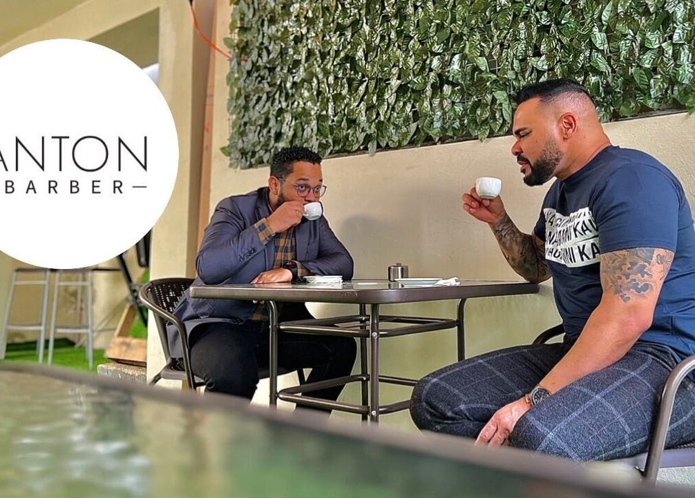 Dos hombres disfrutan café en Anton Barber, Santo Domingo, Distrito Nacional, DO con fondo de plantas verdes.