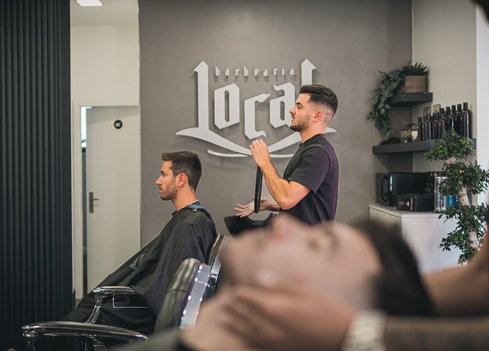 Interior da Barbearia Local - Areal de Cima em Braga, PT, com barbeiro cortando cabelo de cliente.