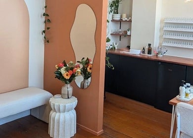 Welcoming interior at Studio Ten, Auckland, NZ featuring a cozy bench, floral decor, and elegant mirror.