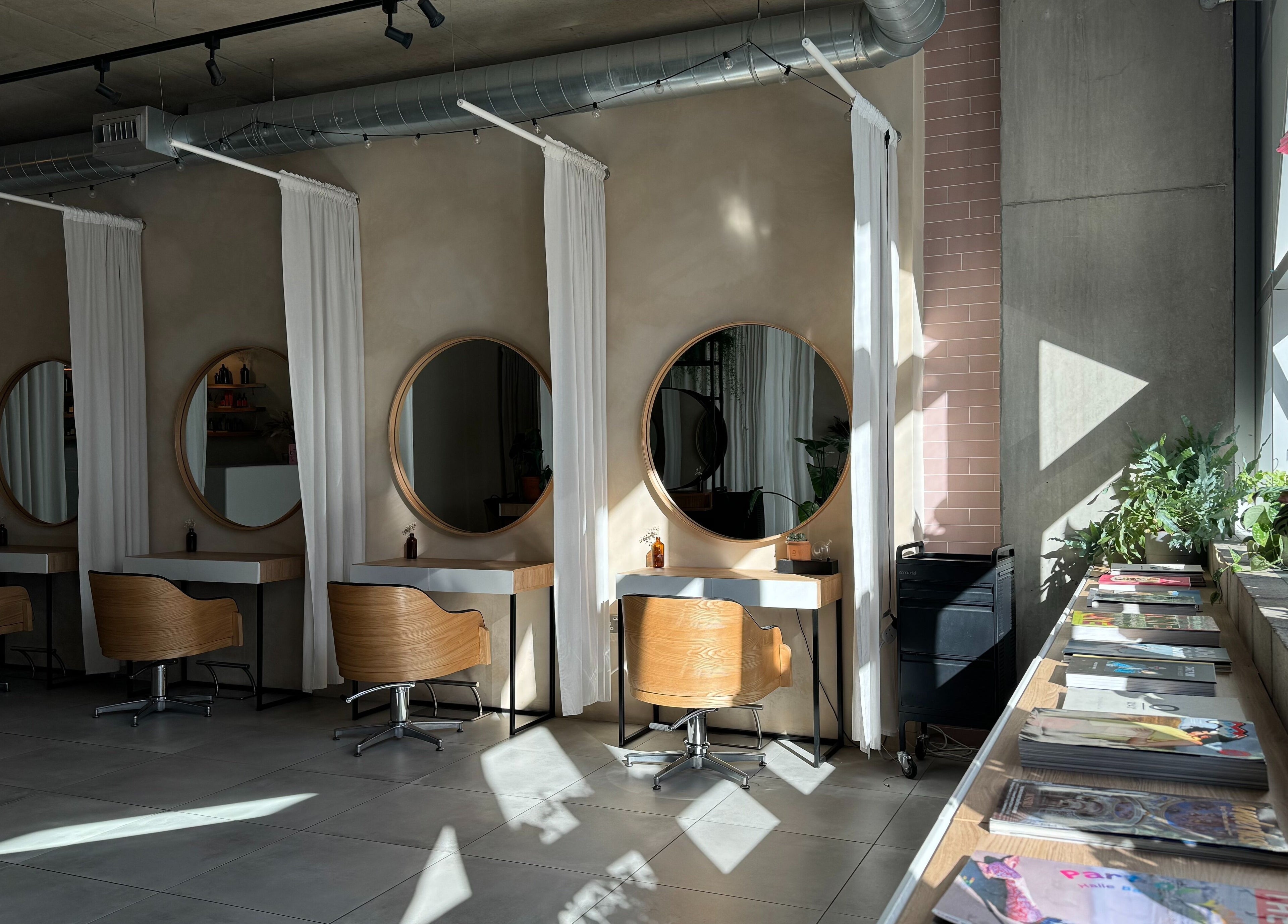 Stylish salon interior at Stanley Watts, London, England, GB featuring round mirrors and wooden chairs.