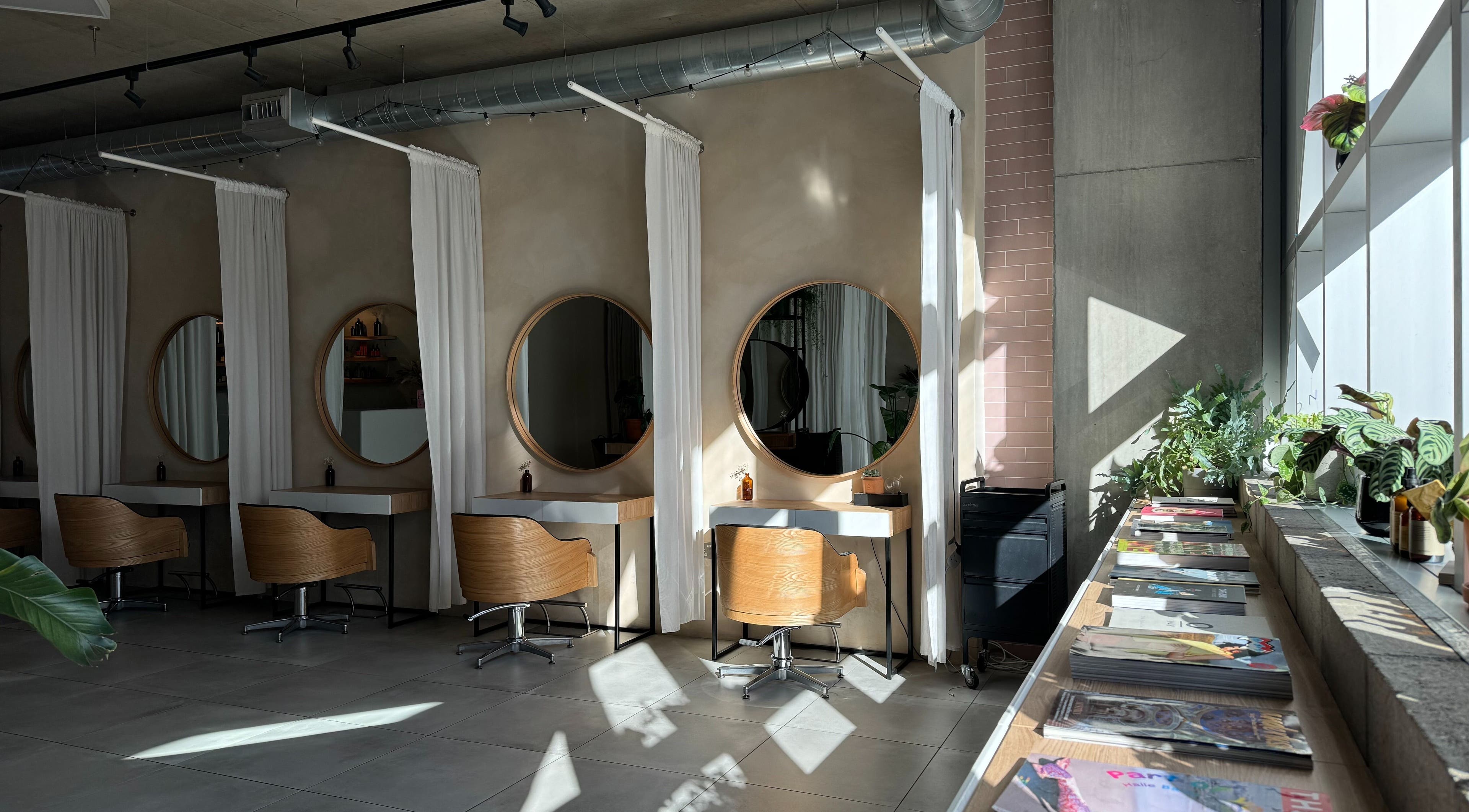 Stylish salon interior at Stanley Watts, London, England, GB featuring round mirrors and wooden chairs.