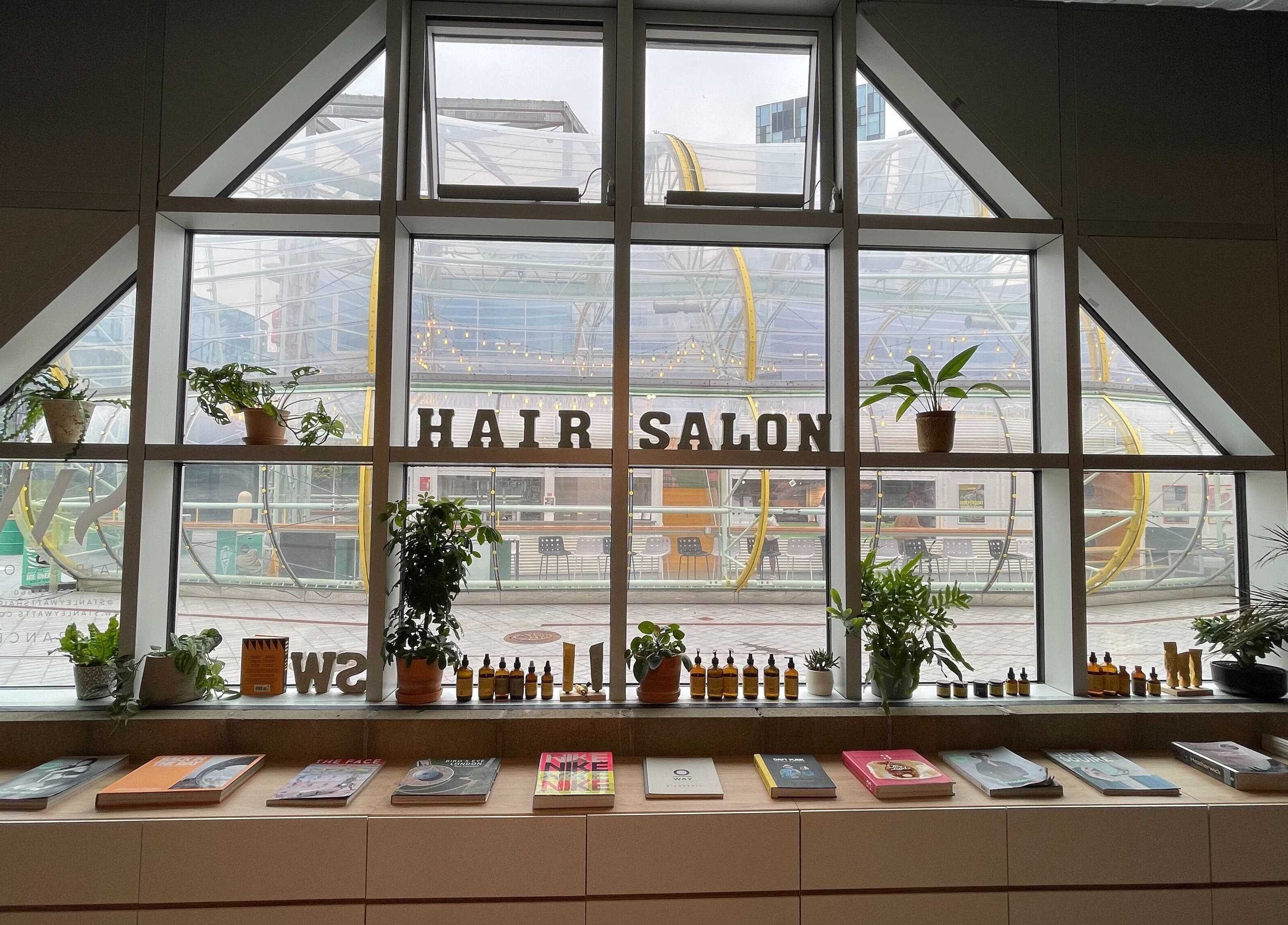 Interior of Stanley Watts hair salon in London, England, GB, featuring a large window with plants and books.