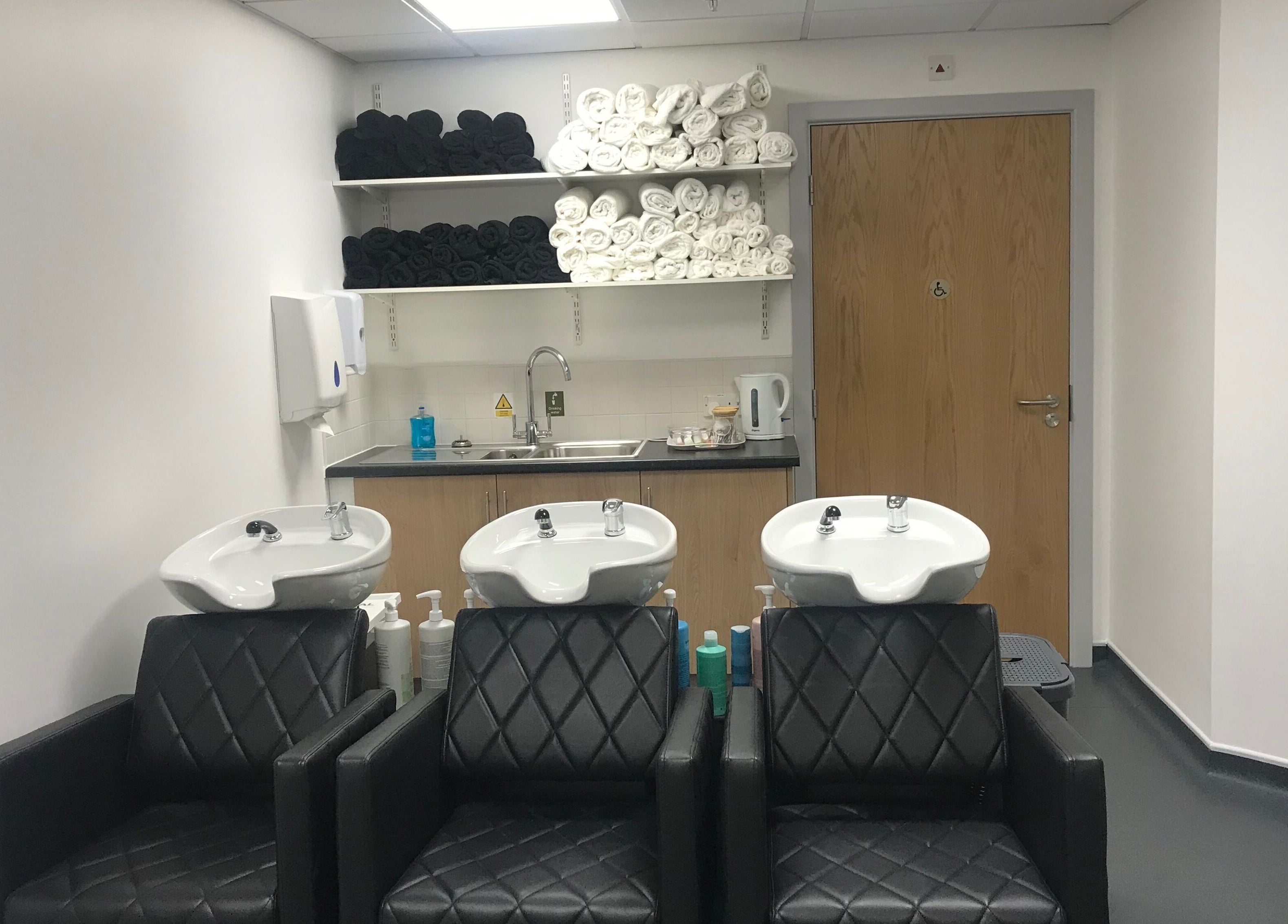 Modern wash area at Skills and Learning Barbering Training Salon in Poole, England, GB featuring black chairs and sinks.