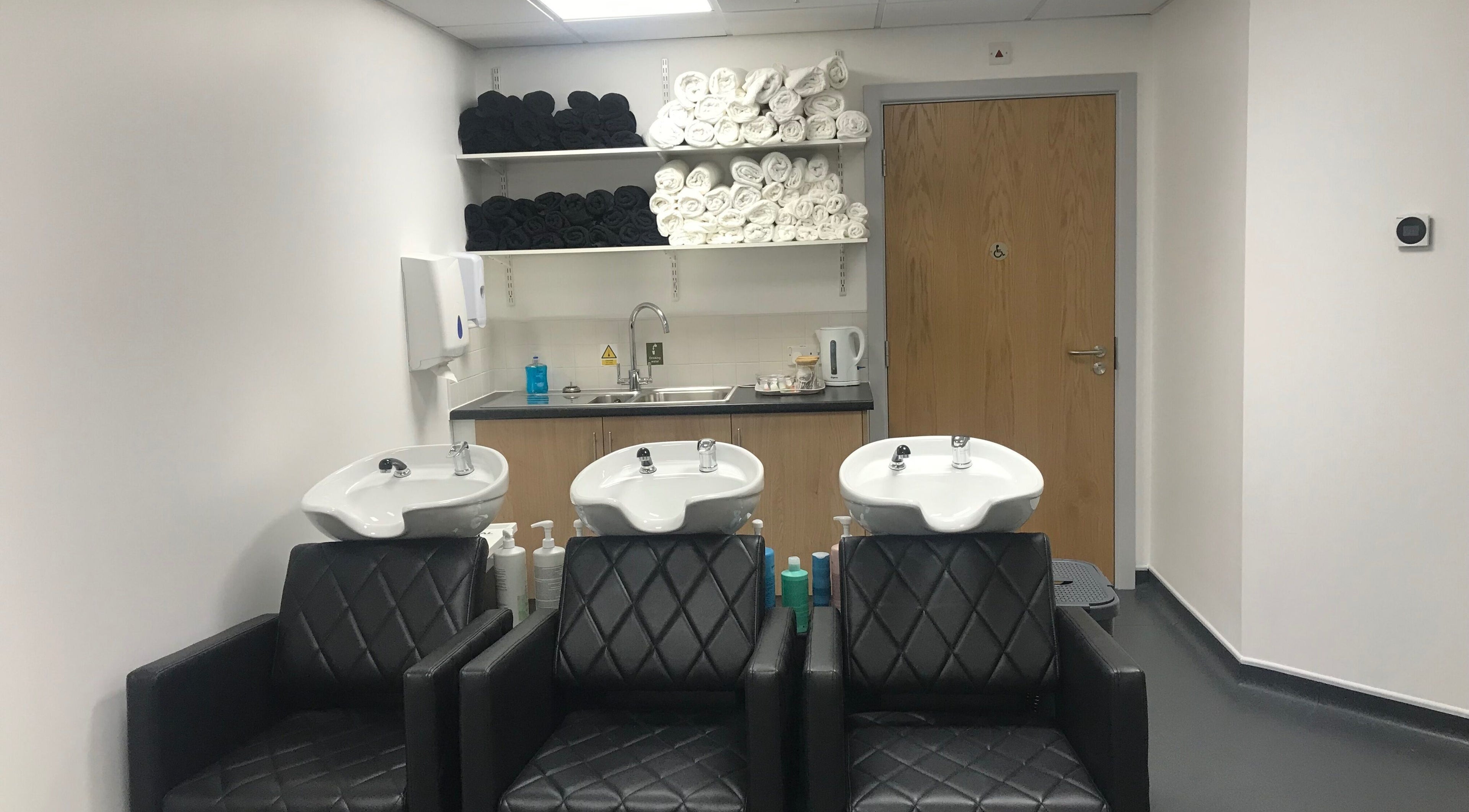 Modern wash area at Skills and Learning Barbering Training Salon in Poole, England, GB featuring black chairs and sinks.