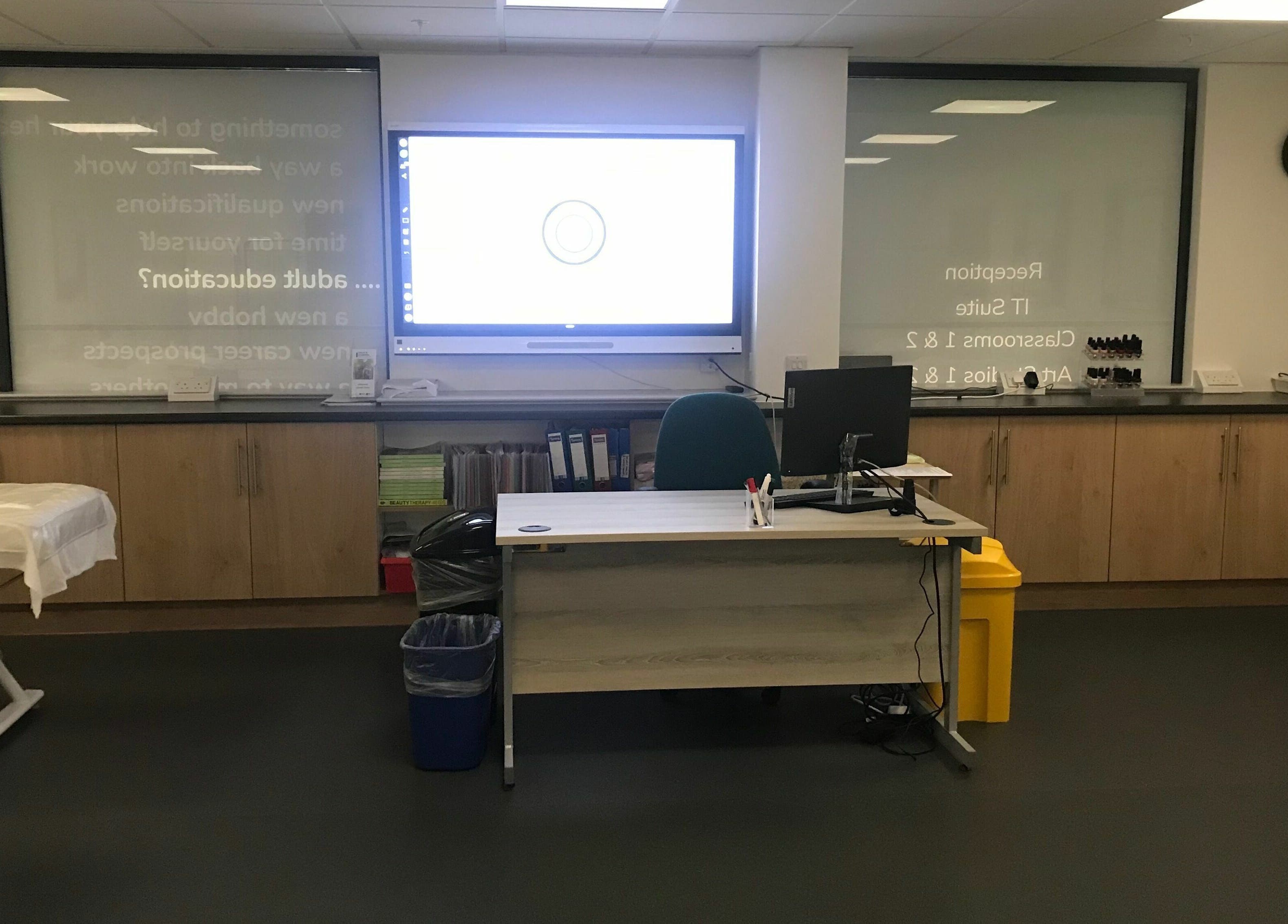 Modern classroom at Skills and Learning Beauty Training Salon in Poole, England, GB, with desks and a display screen.