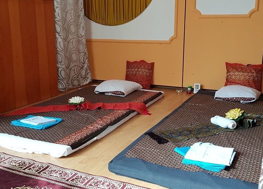 Traditional Thai massage setup at Urai Thai Massage, Budapest, HU with mats, pillows, and decorative flowers.