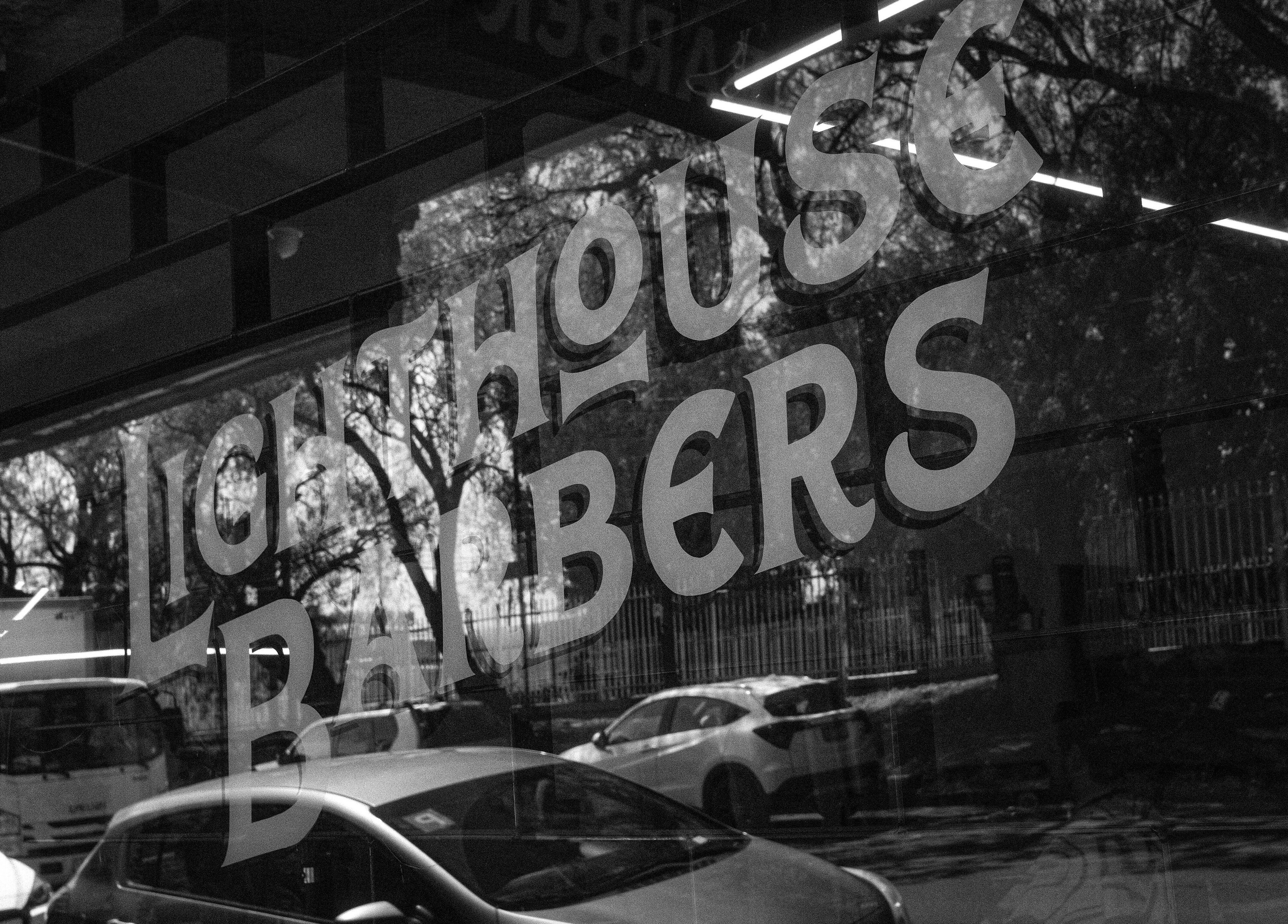 Front window of Lighthouse Barbers in Melbourne, Victoria, AU with logo reflecting the street.