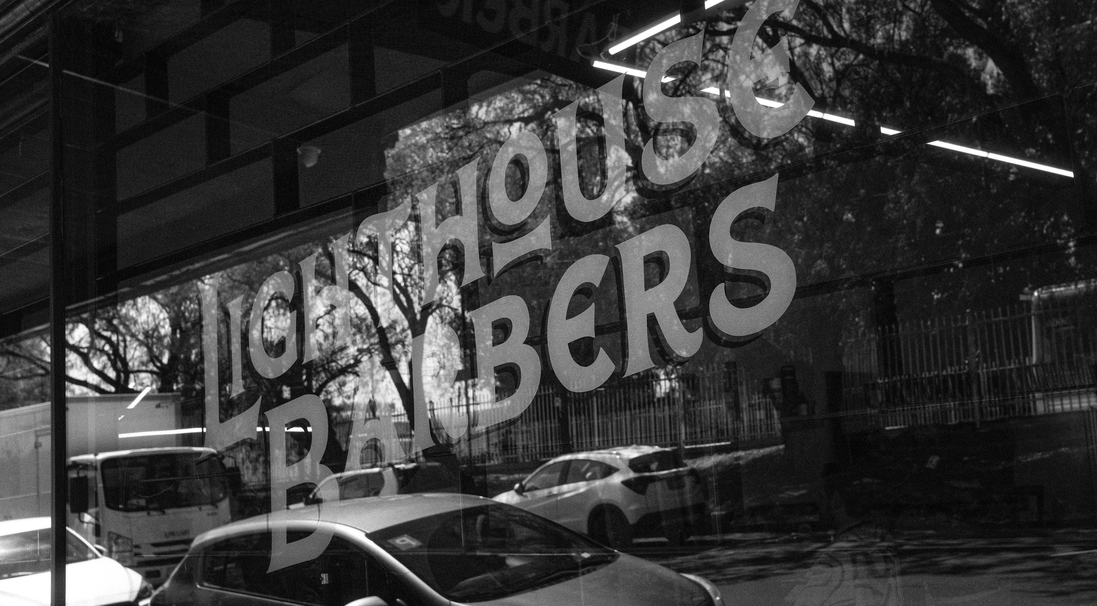 Front window of Lighthouse Barbers in Melbourne, Victoria, AU with logo reflecting the street.