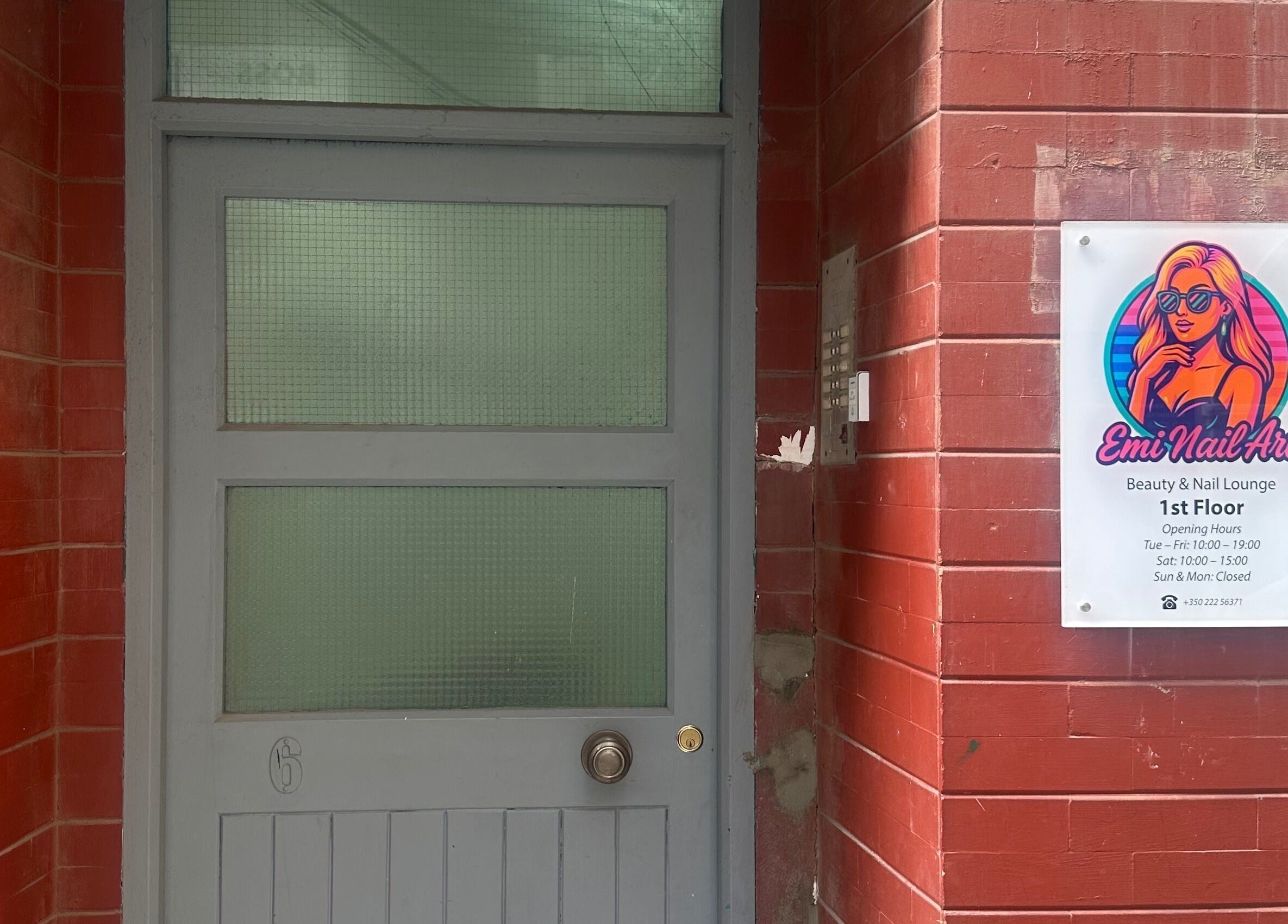 Entrance of Emi Nail Art in Gibraltar, GI with vibrant signage and red brick wall.